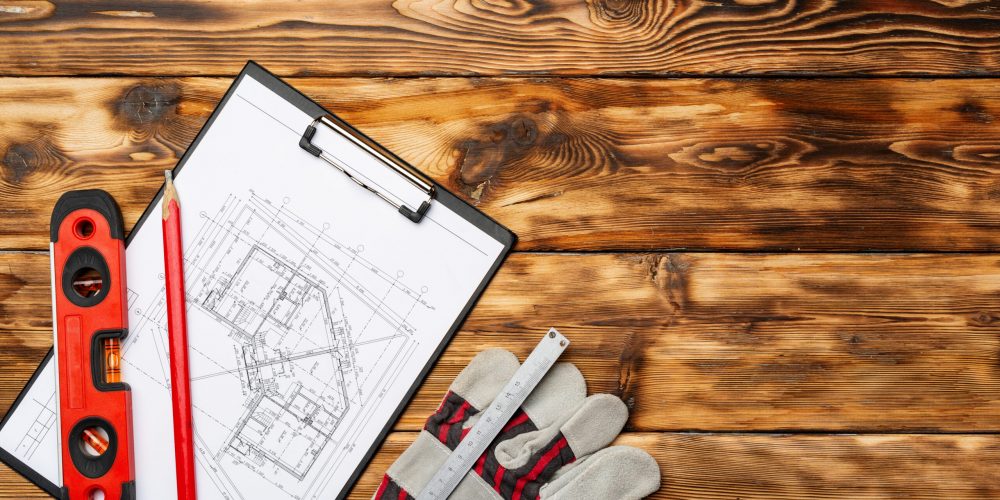 Blueprints, level and gloves of a construction worker on wooden table top view